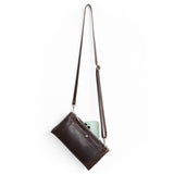 A dark brown leather crossbody bag with a long adjustable strap, shown with a light green smartphone tucked into its side pocket, against a solid white background.