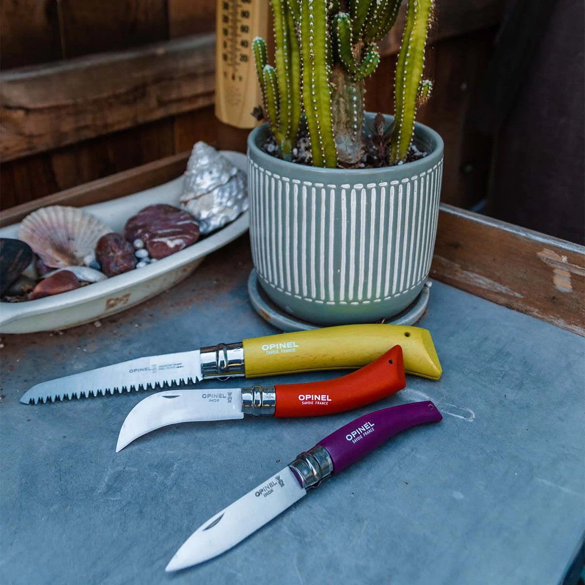 the 3 garden tools included in the set on a garden table alongside a potted cactus