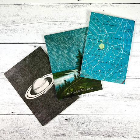 3 celestial themed notebooks with different designs on a wooden surface