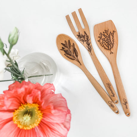 Set of wooden utensils with herb designs and engravings on a white background with flowers.