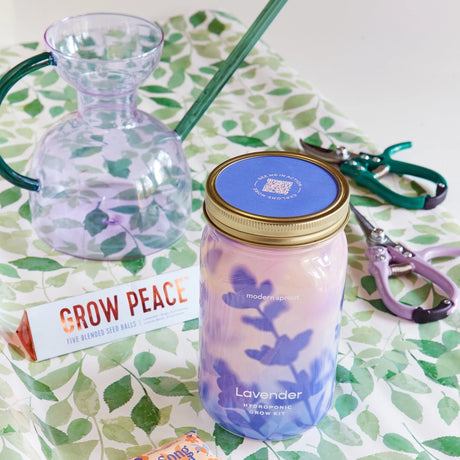 Lavender grow kit with a jar, plant, and tools on a leaf-patterned surface.