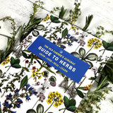Book titled 'The Old Farmer's Almanac Guide to Herbs' surrounded by herbs and flowers on a white background