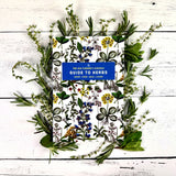 Book titled 'The Old Farmer's Almanac Guide to Herbs' surrounded by various herbs on a wooden surface.