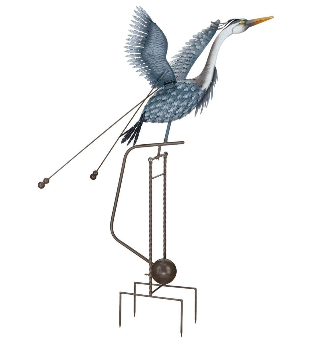 Full view/side angle of a metal heron sculpture in mid-flight, with outstretched wings and an elongated neck. The sculpture features detailed feather patterns and is mounted on a tall, sturdy frame with a spherical weight and pronged legs at the base. Two rods with weights are attached to the bird's body, enhancing its kinetic movement. The heron is painted in shades of blue and gray, and its long yellow beak is pointed forward.