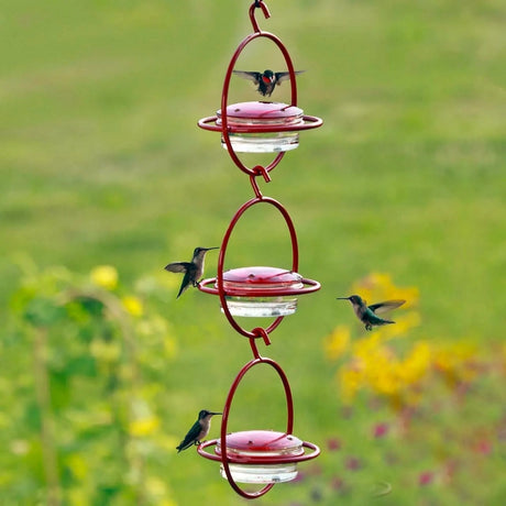 three red hummingbird feeders hanging from one another in a vertical line with 4 hummingbirds flying around them