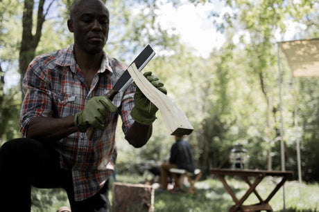 a man at a lush forest campsite splitting firewood with his japanese nata hatchet
