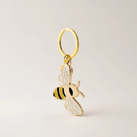 Gold bee-shaped keychain on a light beige background