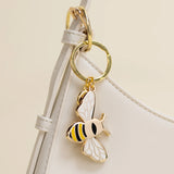 Gold bee-shaped keychain attached to a white strap on a beige background