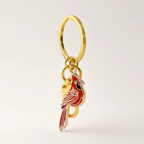 Gold keychain with a red cardinal bird charm on a light beige background