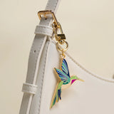 Colorful hummingbird keychain attached to a white strap with a beige background