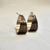 Pair of bronze hoop earrings with leaf-like patterns on a light background