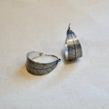 Silver leaf-patterned hoop earring and pendant on a beige fabric background