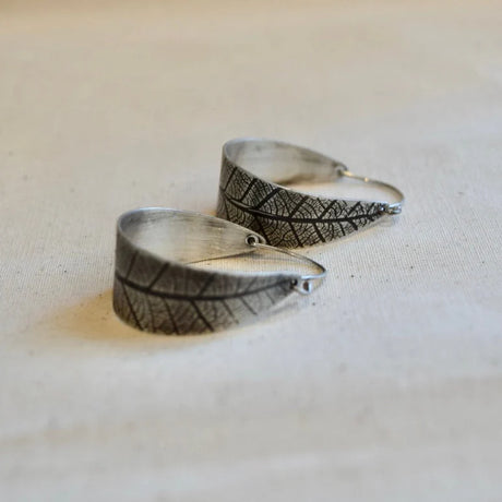 Silver leaf-shaped earrings on a light fabric background