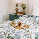 Floral-patterned blanket on a bed with a tray of food and a cup.