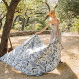Woman setting up a floral-patterned picnic blanket outdoors.