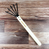 long handle gardening tool with black cultivating tines on a wooden surface