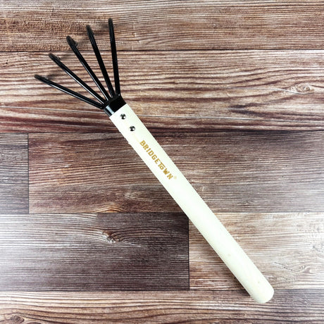 long handle gardening tool with black cultivating tines on a wooden surface