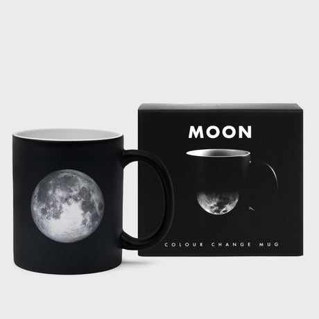 Black color-changing mug with moon design next to its packaging box on a light gray background