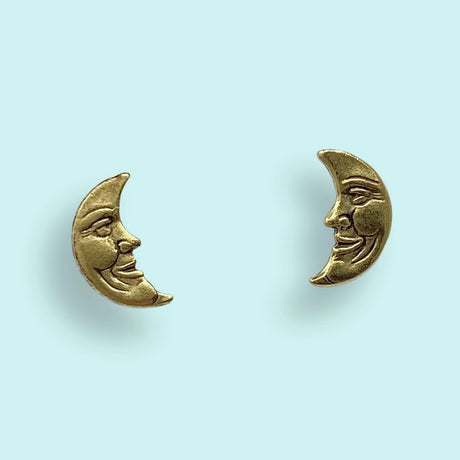 Gold crescent moon-shaped earrings with face designs on a light blue background