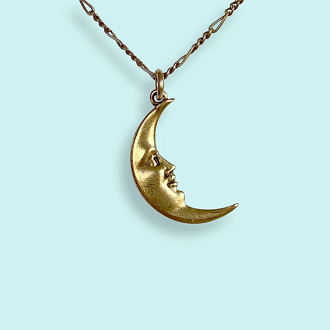 Gold crescent moon necklace with face design on a light blue background