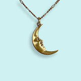 Gold crescent moon necklace with face design on a light blue background