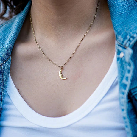 Gold necklace with a moon pendant worn by a person in a denim jacket and white shirt.