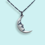 Silver moon-shaped pendant necklace on a light blue background