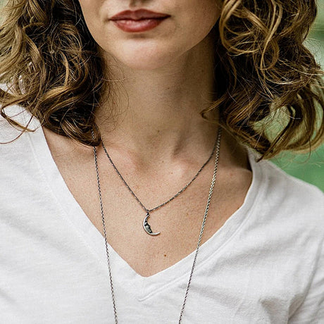 Close-up of a person wearing a necklace with a moon pendant, against a blurred natural background.