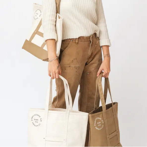 Person holding multiple tote bags with a visible brand logo on a white background