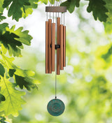 Bronze wind chime with a green disc against a blurred green leafy background