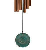 Decorative wind chime with a turquoise disc and copper tubes on a white background