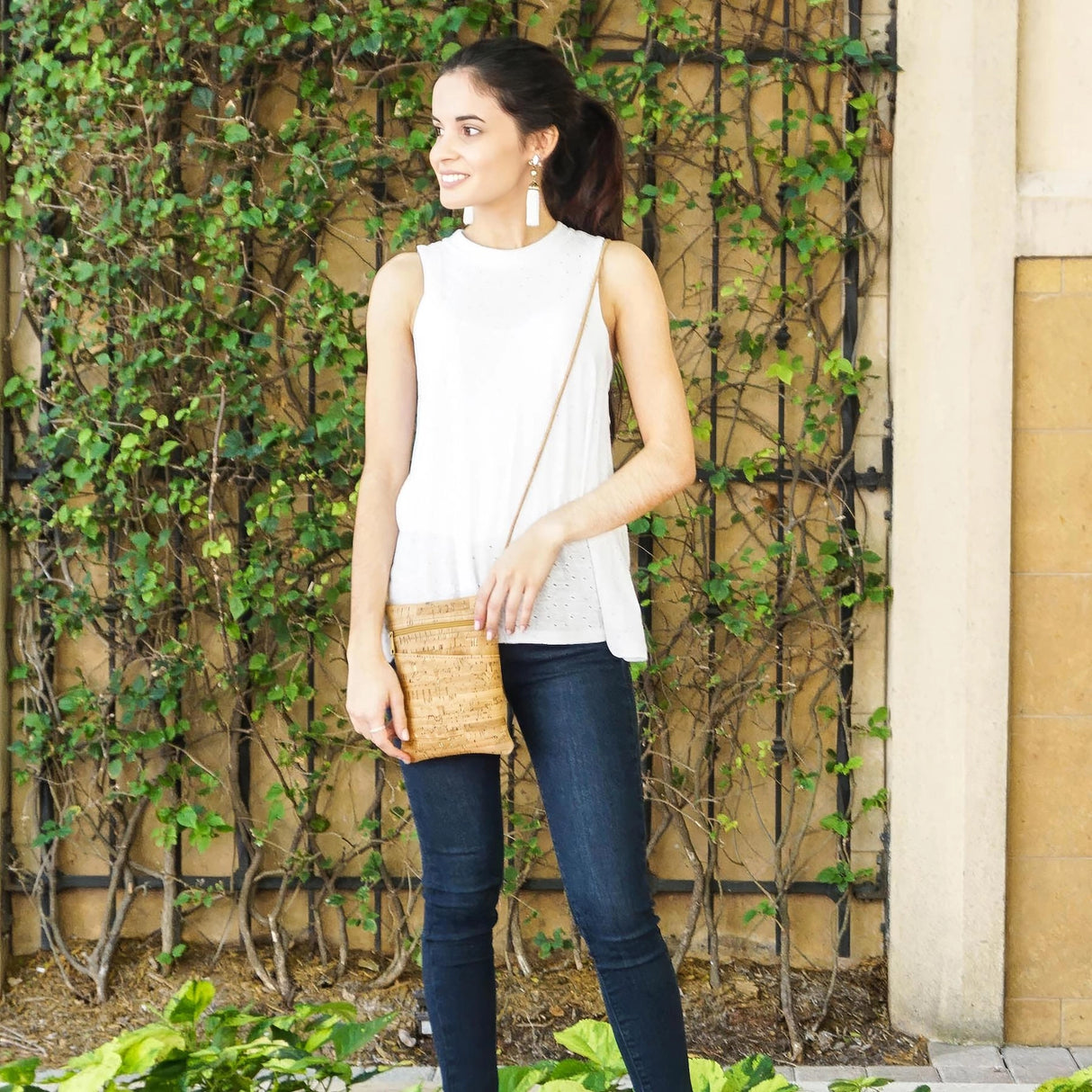 Woman wearing the gold fleck cork mini crossbody bag in front of a green ivy-covered wall.
