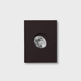 Black book with a circular cutout displaying the moon on a light gray background