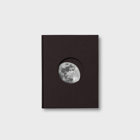 Black book with a circular cutout displaying the moon on a light gray background