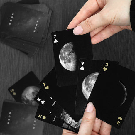 Black playing cards with moon phases held by a hand on a dark surface
