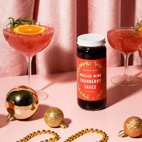 Mulled wine cranberry sauce bottle with cocktails and Christmas ornaments on a pink background