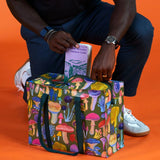 Person holding a colorful mushroom-patterned bag against an orange background