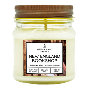 a candle in a clear glass mason jar with off white wax and a label that reads "New England Bookshop" against a white background