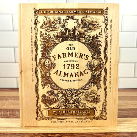 The Old Farmer's Almanac book on a wooden surface with a white tiled wall background