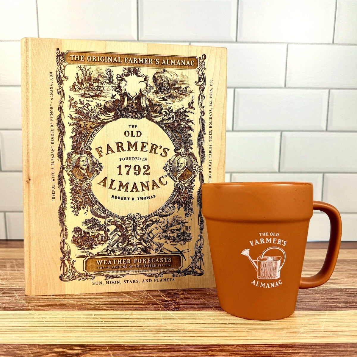 The Old Farmer's Almanac cutting board and a matching mug on a wooden surface with a white tiled wall background.