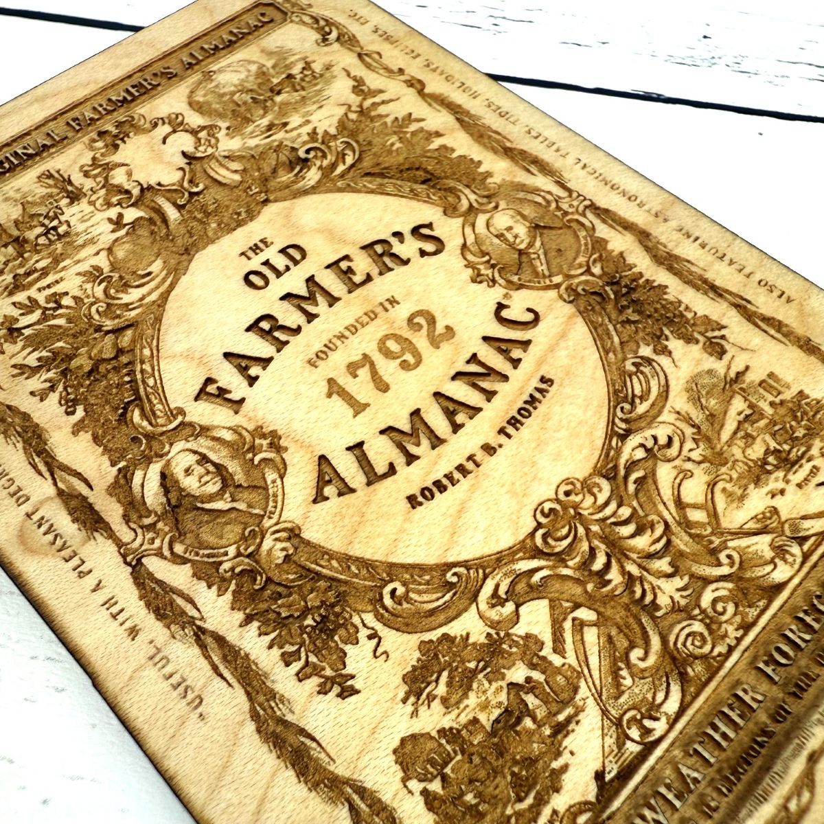close up of 'The Old Farmer's Almanac' wooden ornament with decorative elements on a wooden surface.