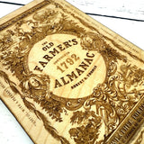 close up of 'The Old Farmer's Almanac' wooden ornament with decorative elements on a wooden surface.