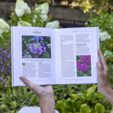Person holding a book about flowers with images of hydrangeas against a garden background