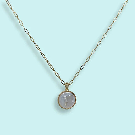 Gold necklace with a round pearl moon face pendant on a light blue background