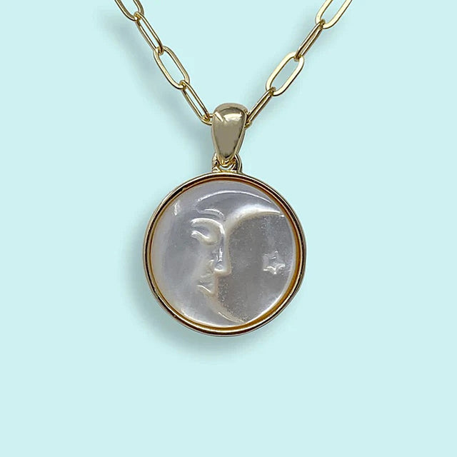 Gold necklace with a circular pendant featuring a crescent moon face design in pearl on a light blue background