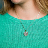 Person wearing a gold necklace with a round pendant on a teal sweater