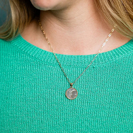 Person wearing a gold necklace with a round pendant on a teal sweater