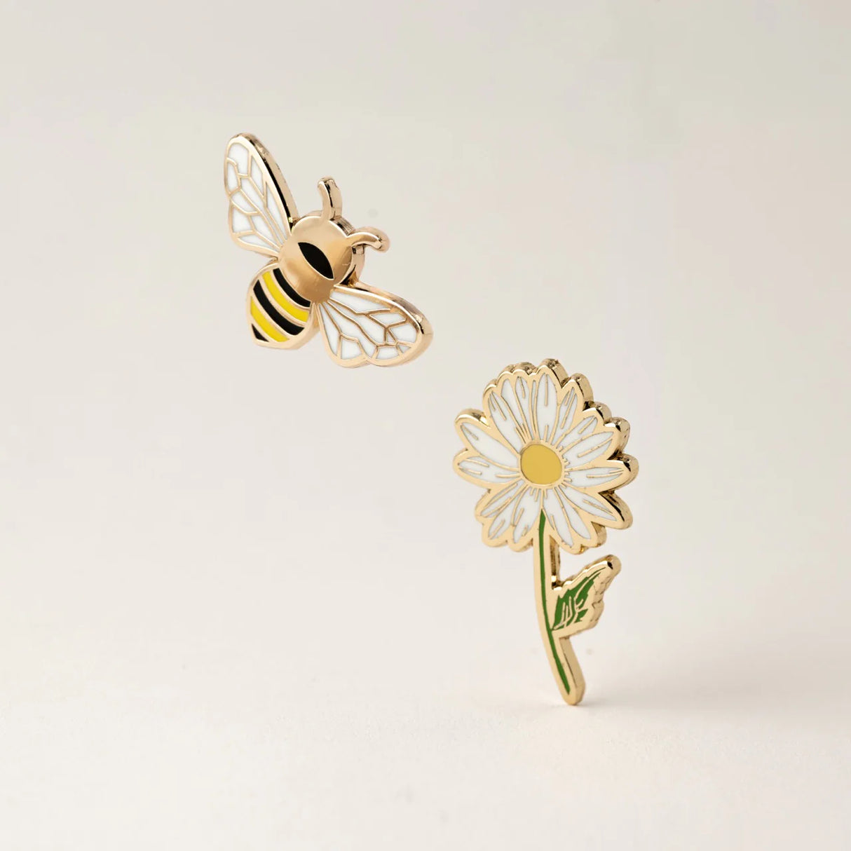 Gold bee and daisy flower enamel pins on a light beige background