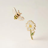 Gold bee and daisy flower enamel pins on a light beige background