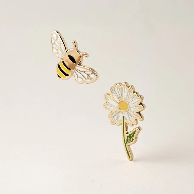 Gold bee and daisy flower enamel pins on a light beige background